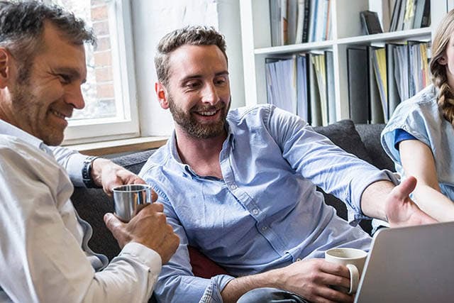 To mænd ser på en PC i sofaen.